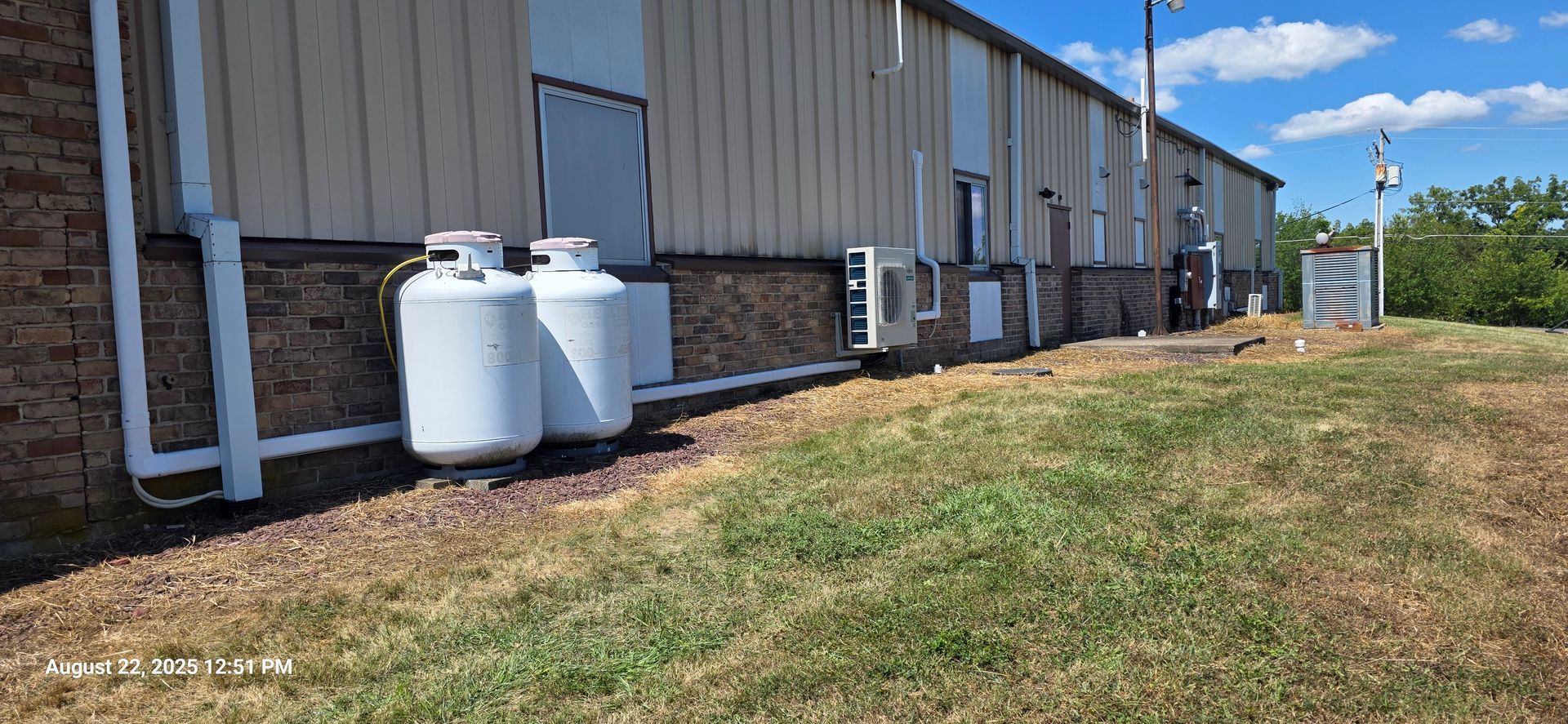 A building exterior with propane tanks, a brick base, and a grassy area under a blue sky.