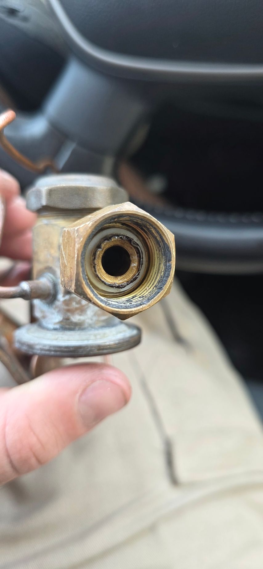 Close-up of a brass fitting with visible threads and interior corrosion, held by a person.