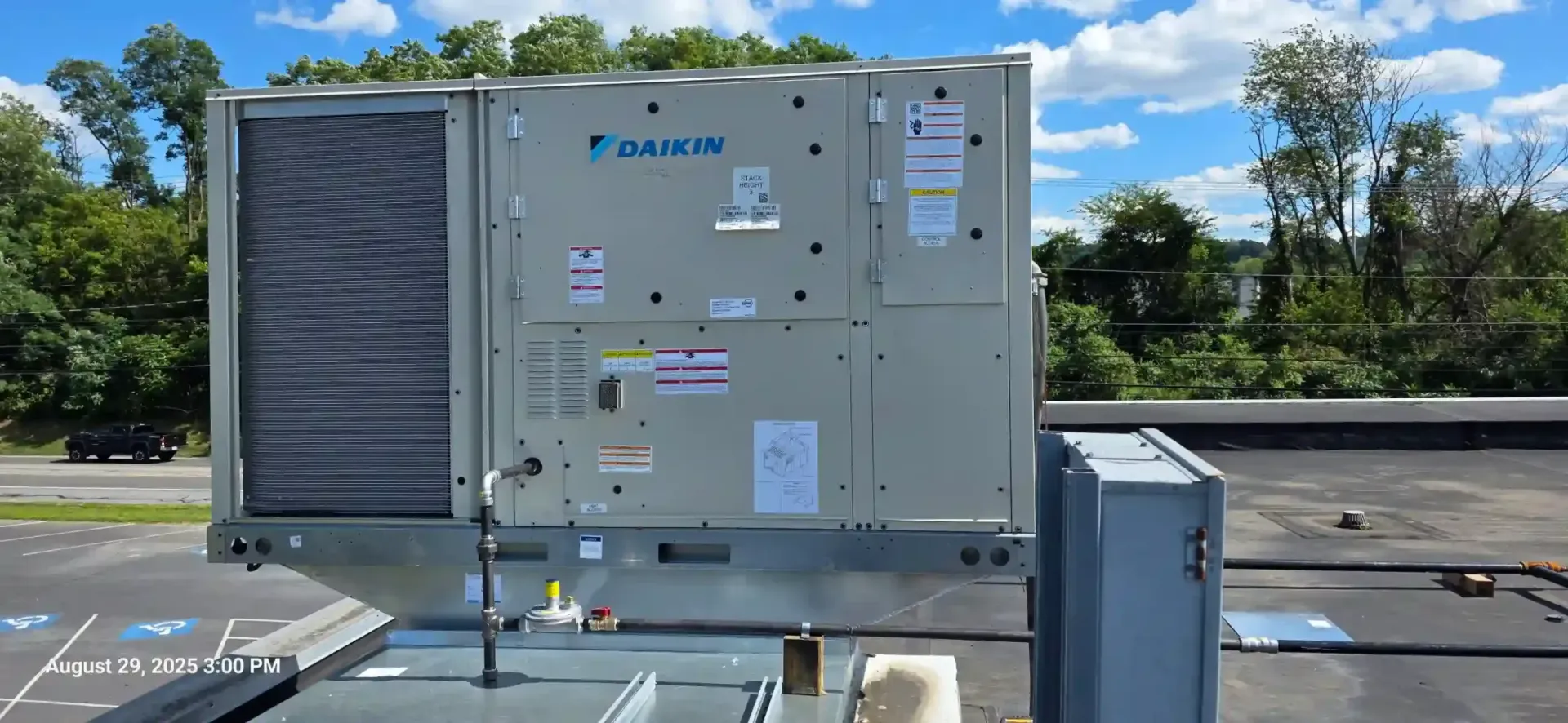 Daikin rooftop HVAC unit on a flat roof against a blue sky with clouds.