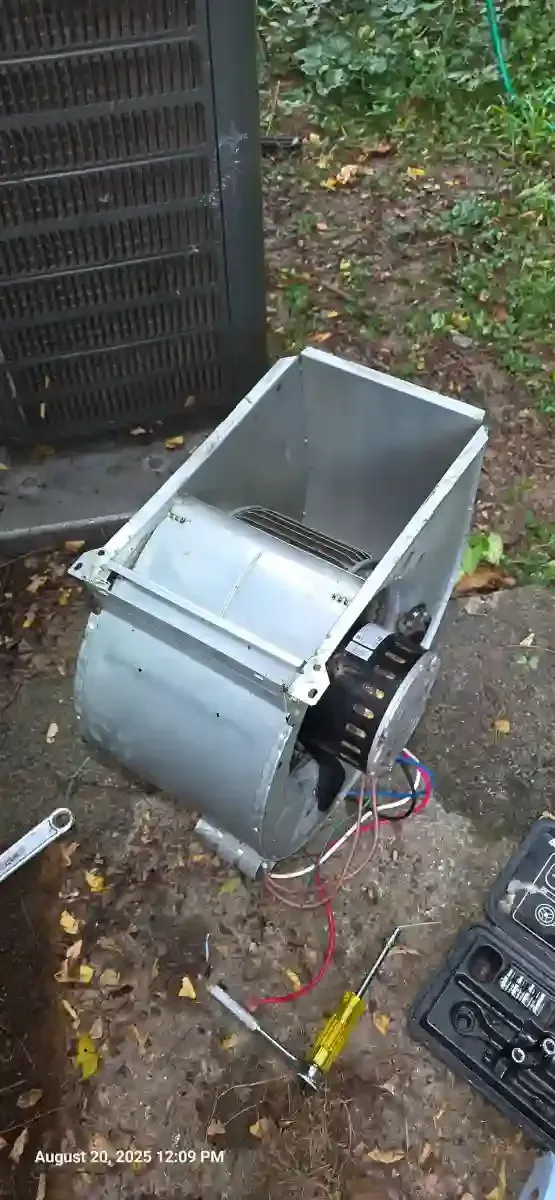 A disassembled metal component, possibly from an air conditioning unit, on a dirt surface. Tools are scattered around.