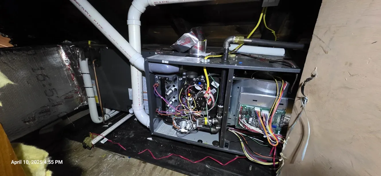 HVAC unit with exposed wiring in an attic setting. Includes ductwork, pipes, and electrical components.