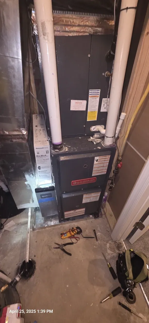 A furnace in a basement.  White PVC pipes and tools on the floor are in view.