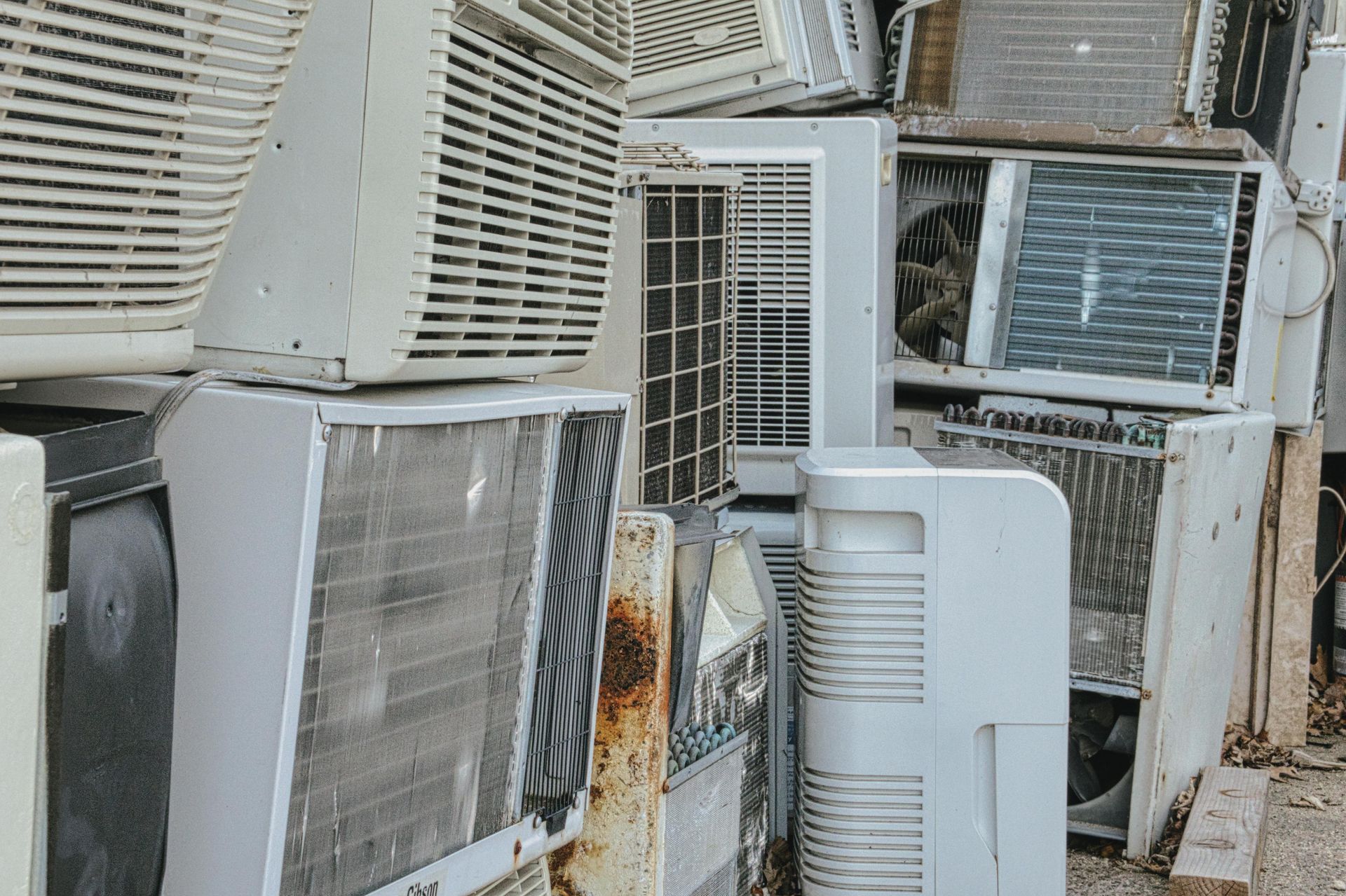 Pile of old, discarded air conditioning units, mostly white, with rusty metal visible.