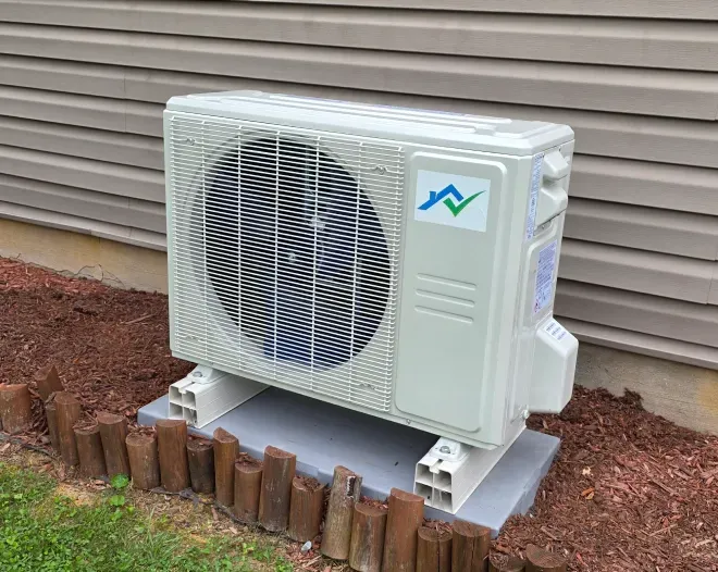 An outdoor air conditioning unit on a concrete pad near a wall with beige siding. Brown edging surrounds the unit.