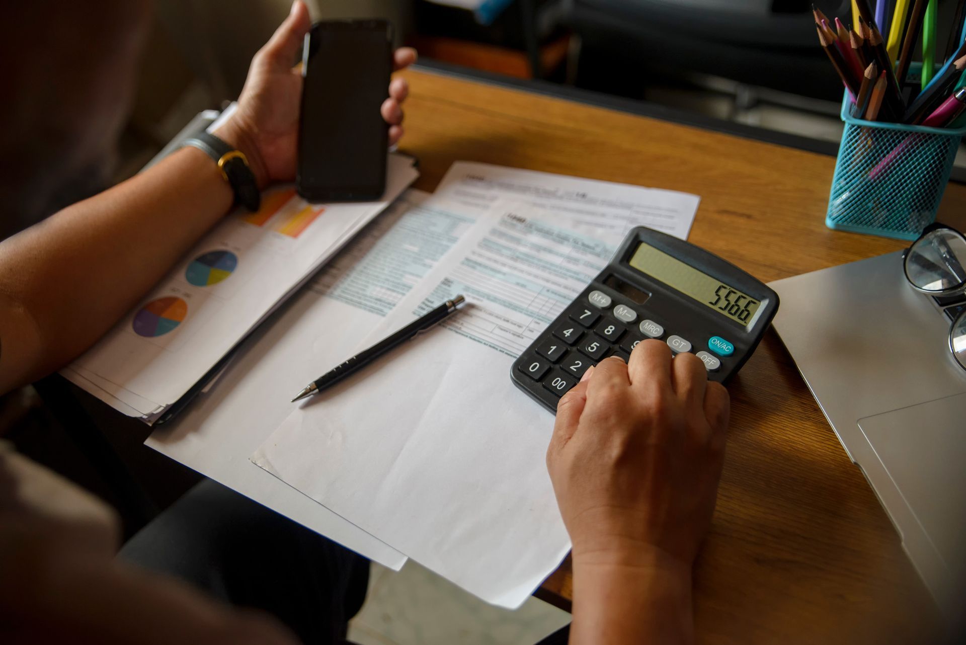 A person is using a calculator while holding a cell phone.
