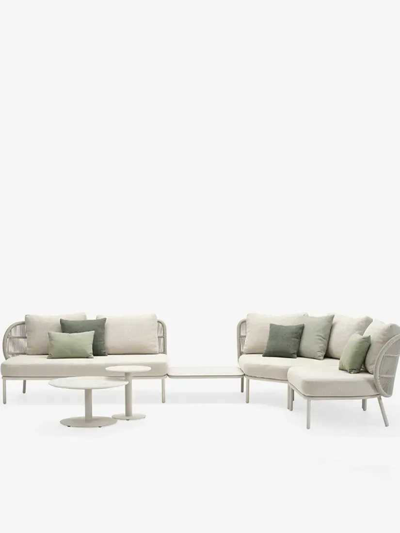 A modular outdoor sofa set in light beige with sage green throw pillows, accompanied by two small round coffee tables.