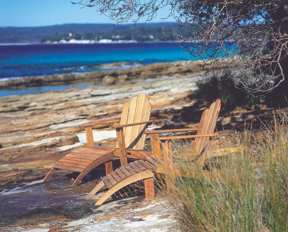 Two Wooden Adirondack Chairs With Footrest on a Rocky Beach — Hastings Specialty Furniture In Port Macquarie, NSW