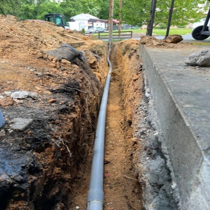A pipe is being installed in a trench next to a sidewalk.