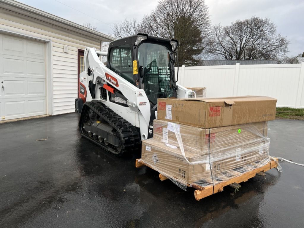 A bobcat is loading boxes onto a wooden pallet in a parking lot.