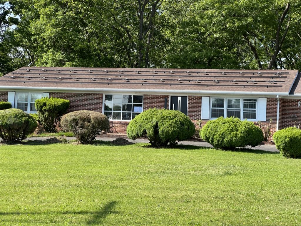 A brick house with a brown roof is sitting on top of a lush green field.