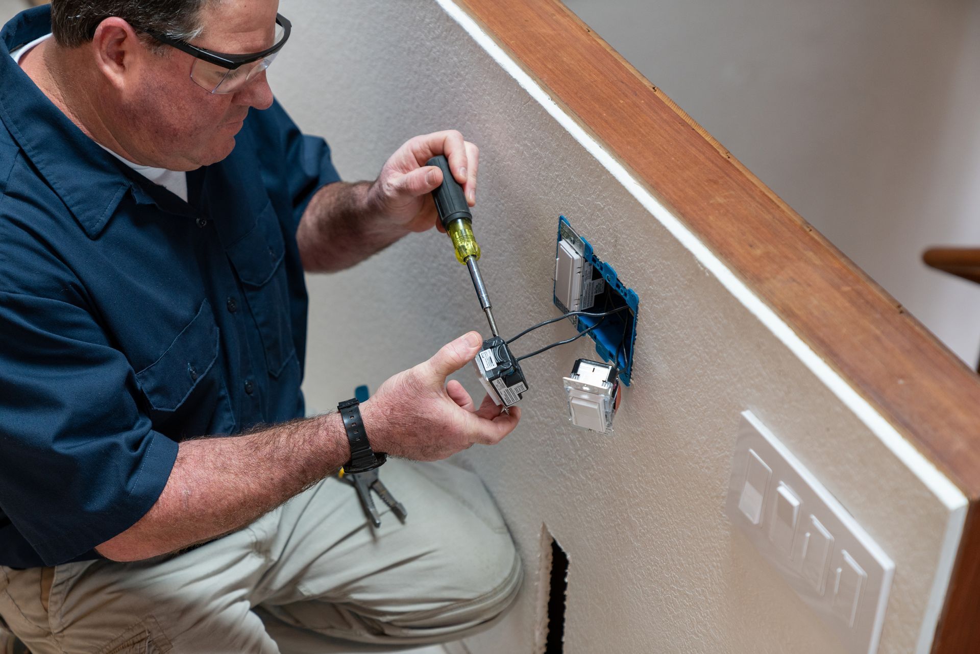 A man is working on a light switch on a wall.