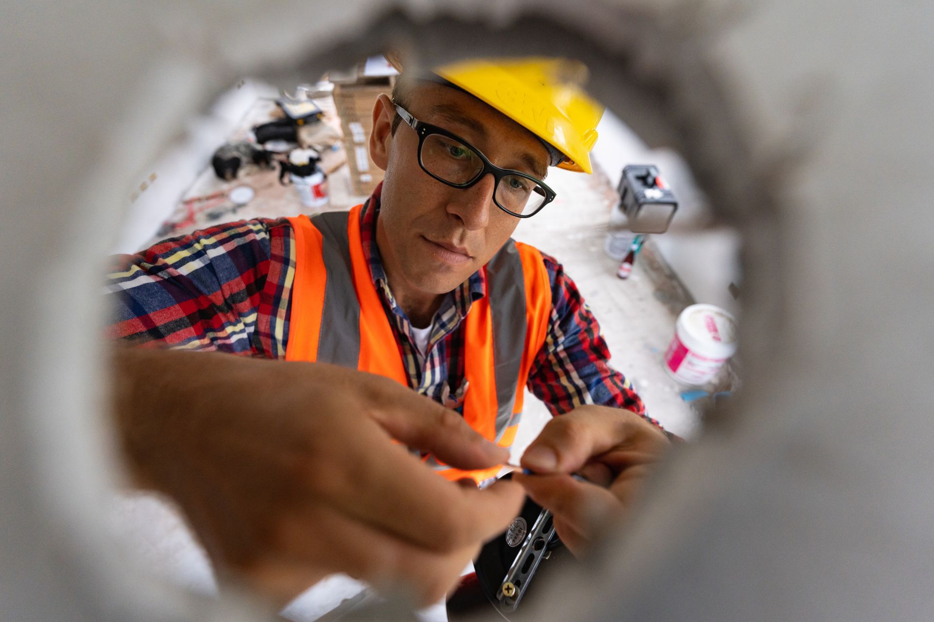 A man wearing a hard hat and safety vest is working on a pipe.
