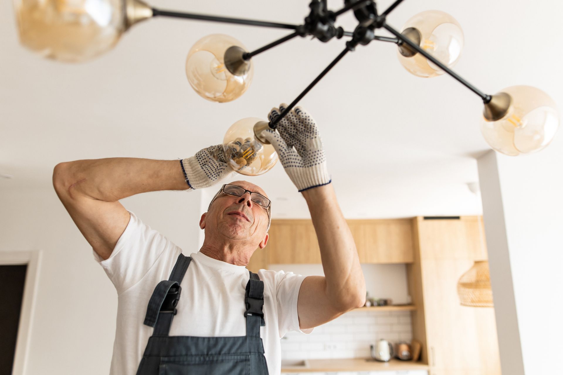 A man is fixing a light fixture in a kitchen.