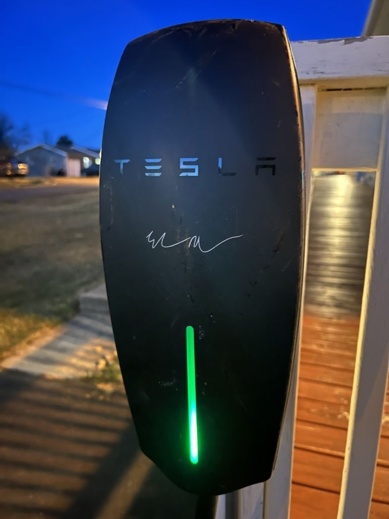 A black tesla charging station with a green light
