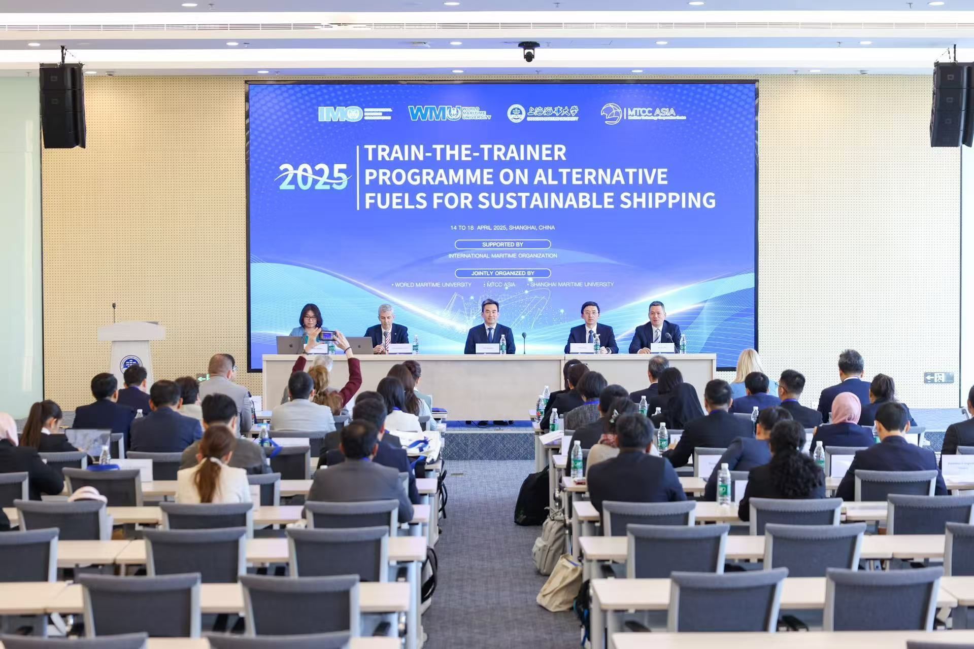 Conference on alternative fuels for sustainable shipping. Presenters at a table, audience in rows of seats.