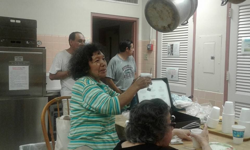 People gathered indoors, one woman raises a cup. Kitchen setting, soft lighting.