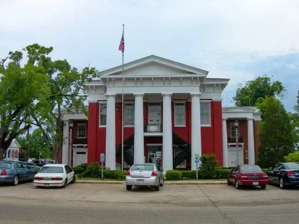 Red brick building with white columns and US flag; cars parked in front.