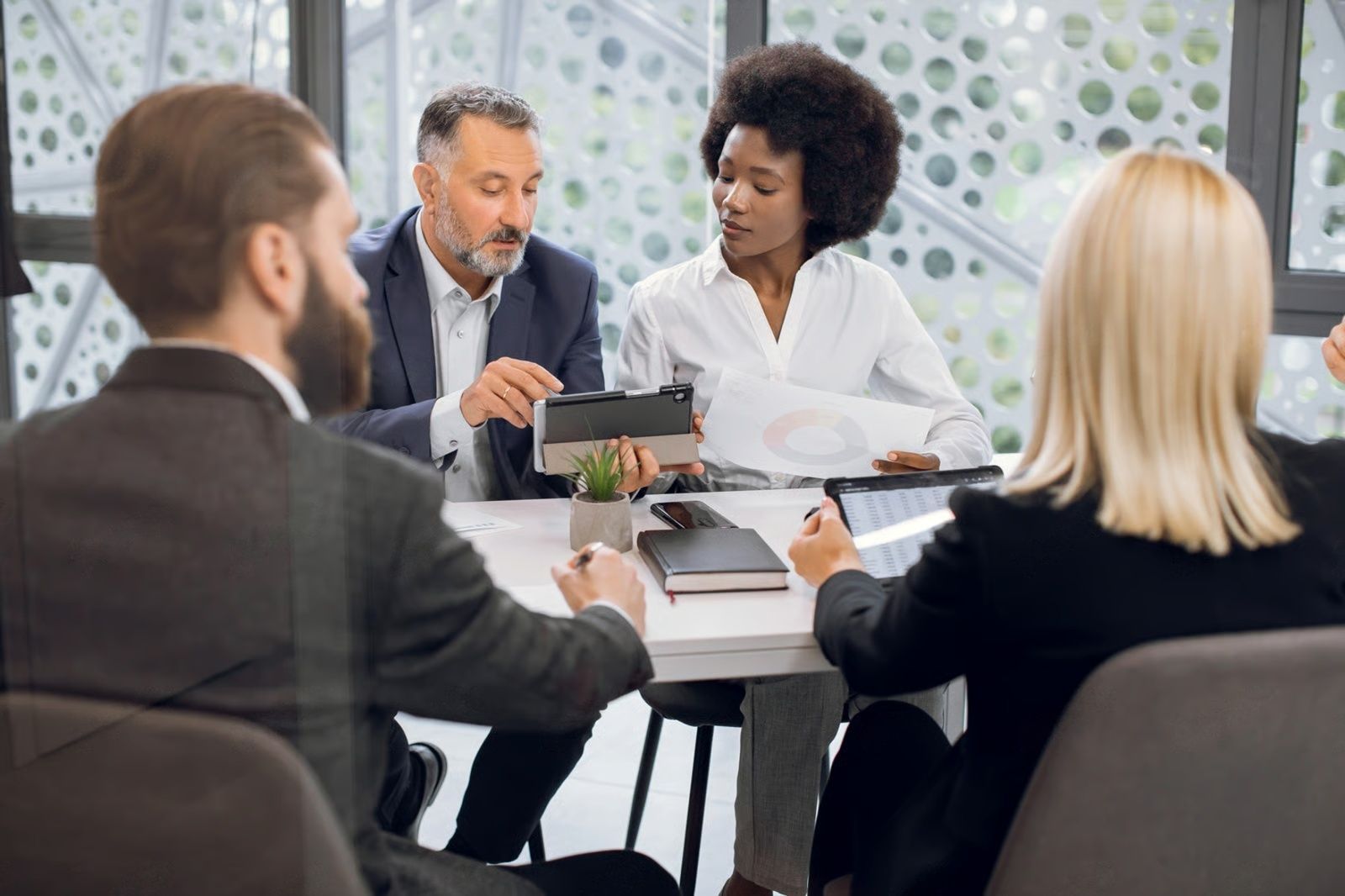 Four people in business attire at a table, reviewing documents and a tablet in an office setting.