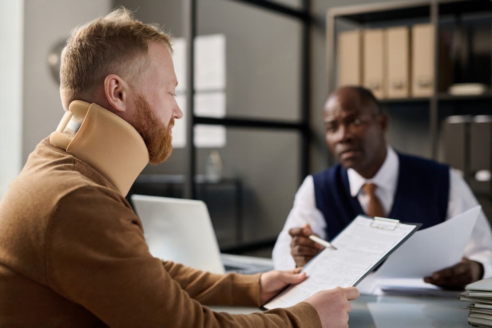 Man in neck brace reviews documents with a person in an office setting.