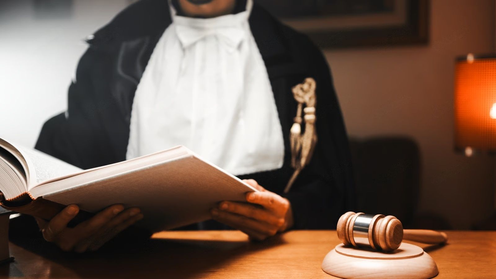 Judge in a courtroom, reading a book, gavel on desk.