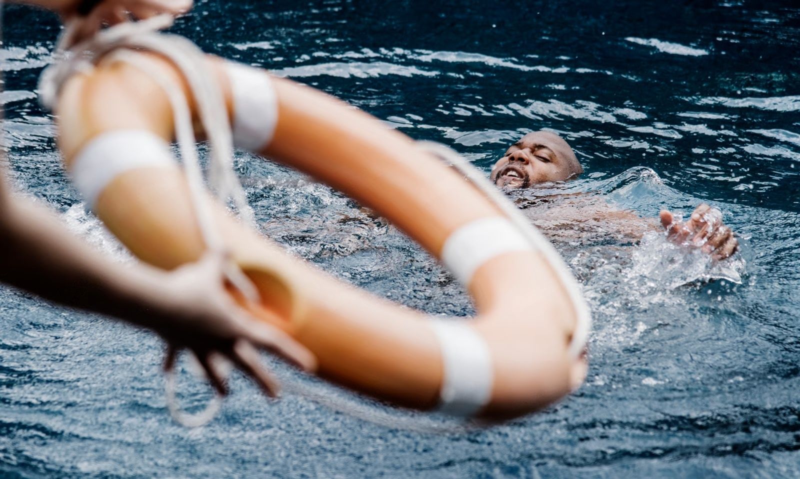 Person in water reaching for a life preserver being held by a person with blurred arms.