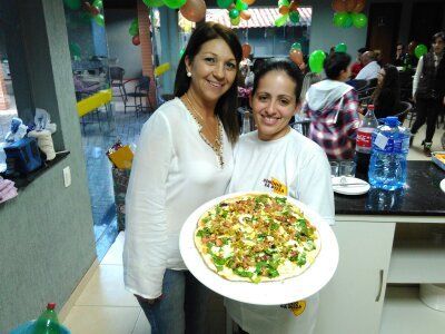 Duas mulheres de pé uma ao lado da outra segurando uma pizza