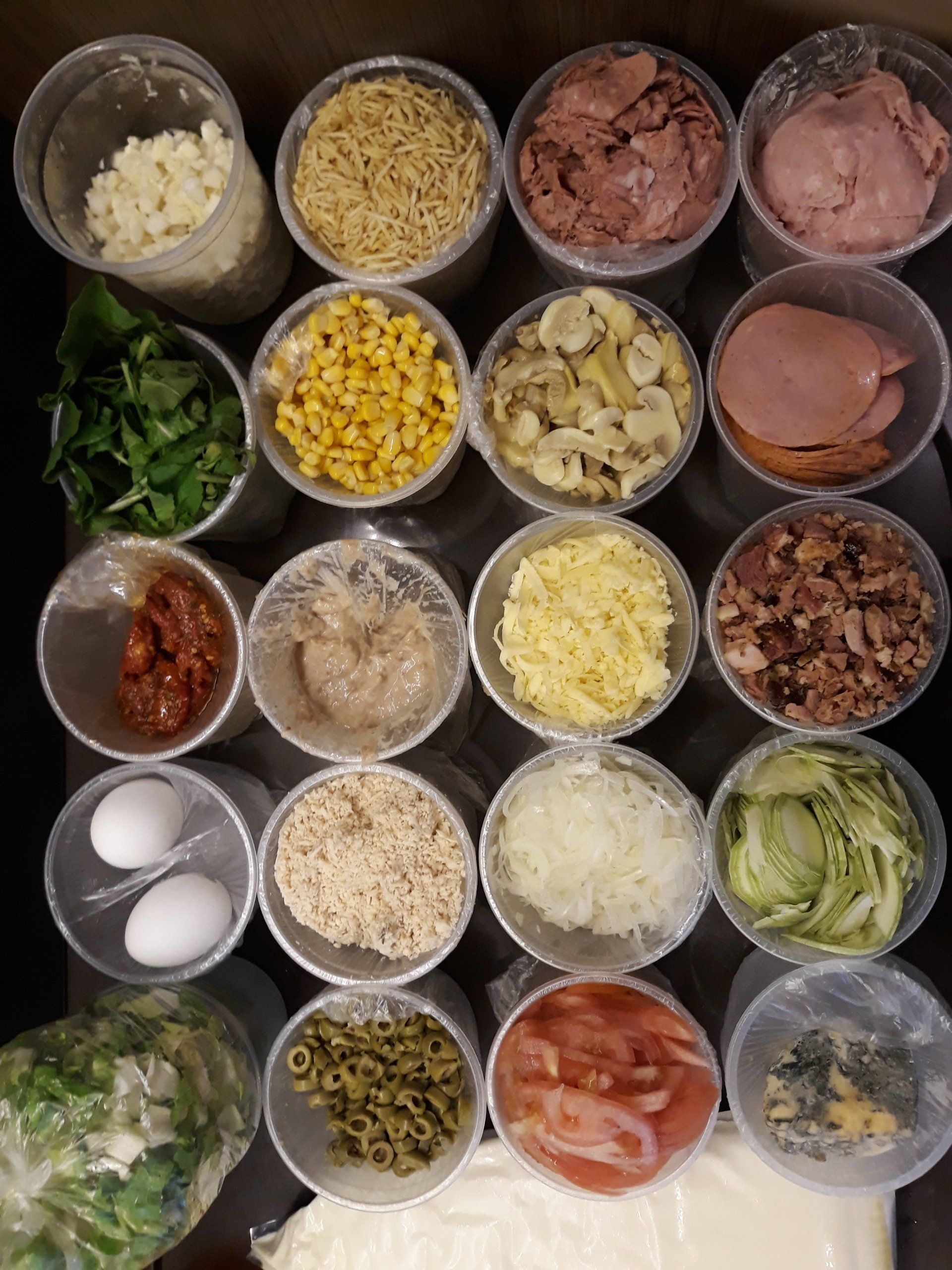 Uma variedade de coberturas estão em copos plásticos sobre uma mesa.