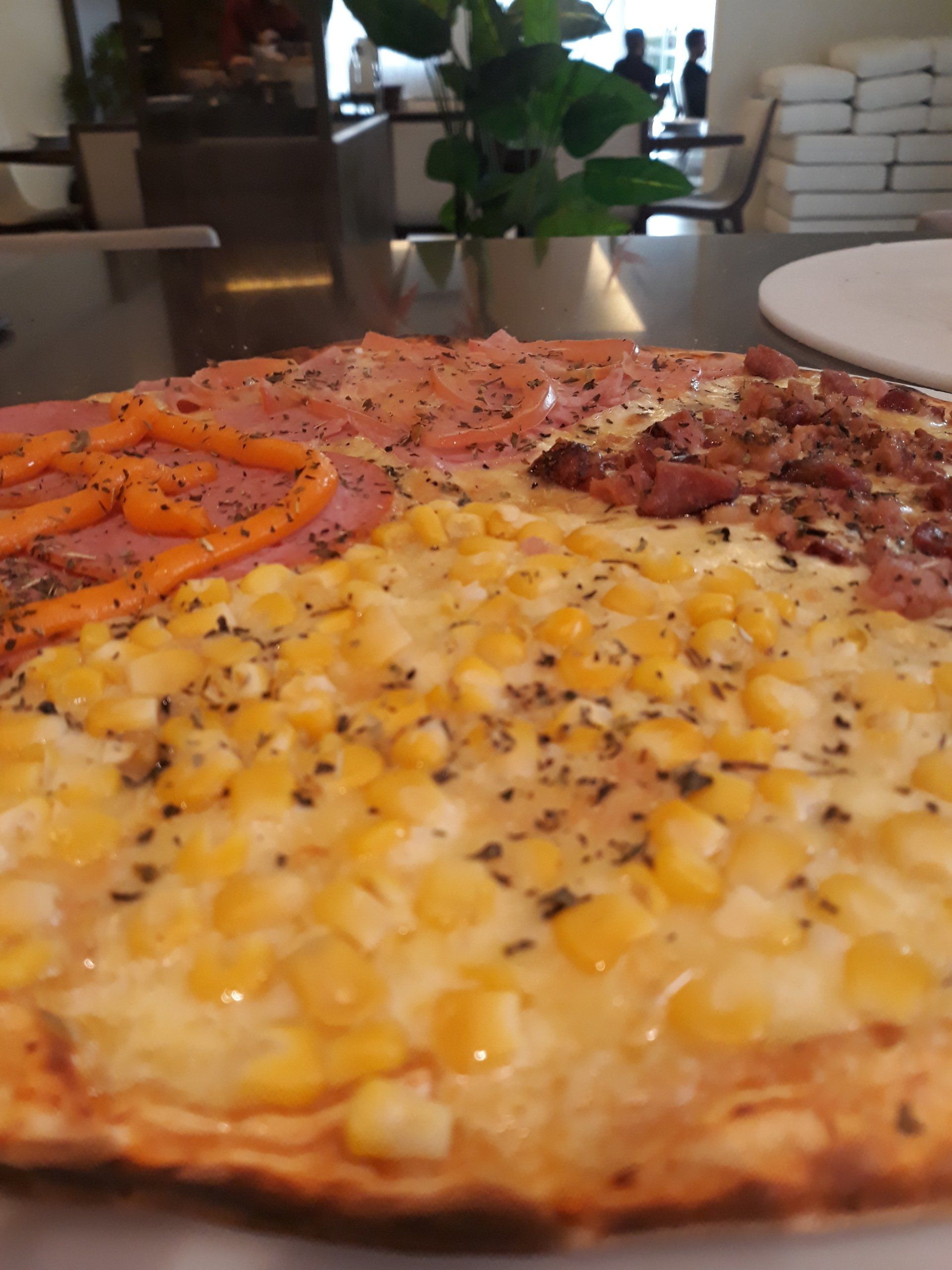 Uma pizza com milho e presunto está sobre uma mesa