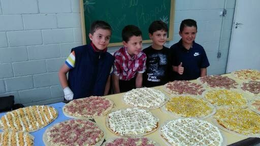 Um grupo de jovens rapazes estão em volta de uma mesa cheia de pizzas.