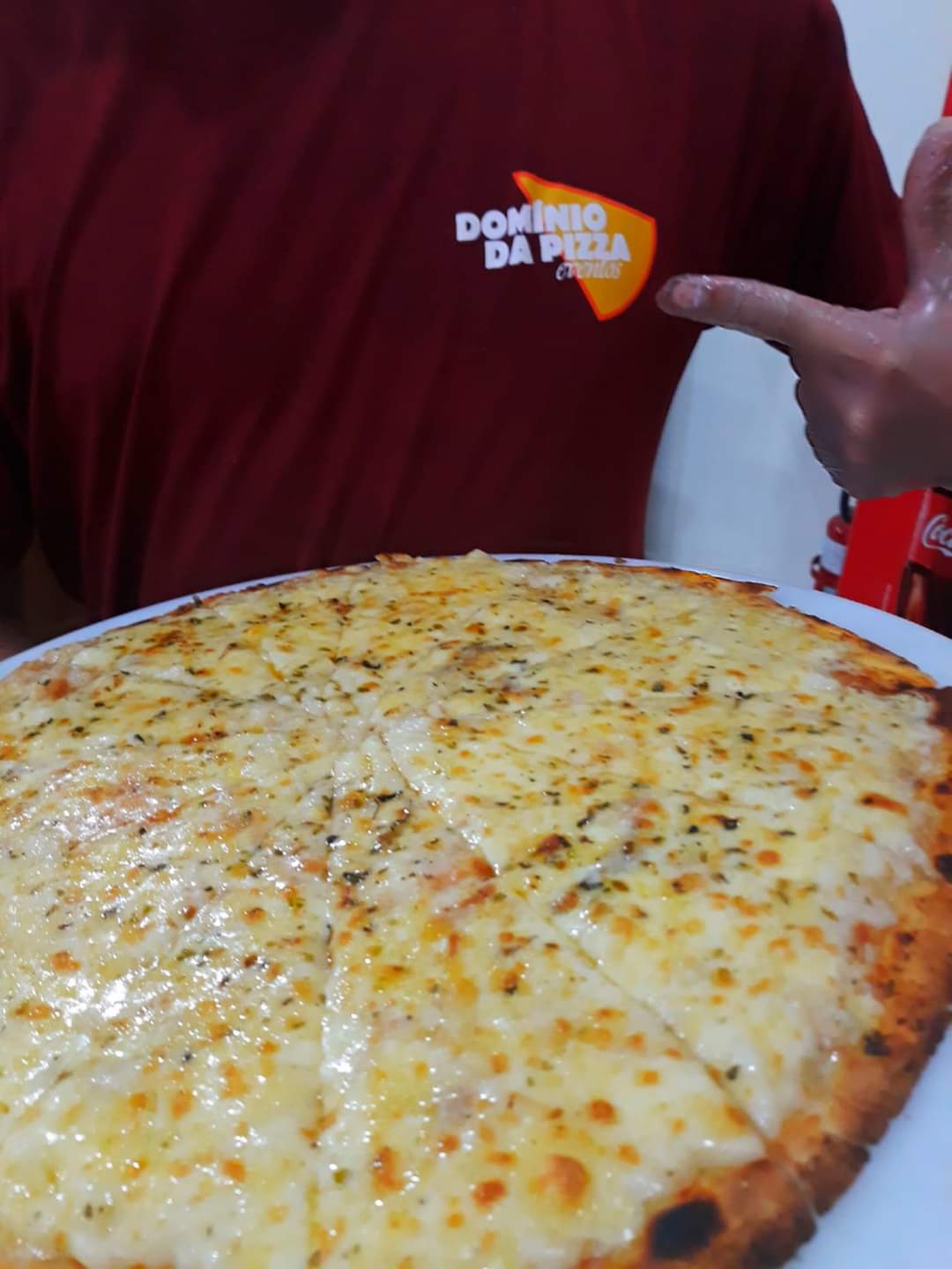 Uma pessoa vestindo uma camisa domino da pizza aponta para uma pizza em um prato