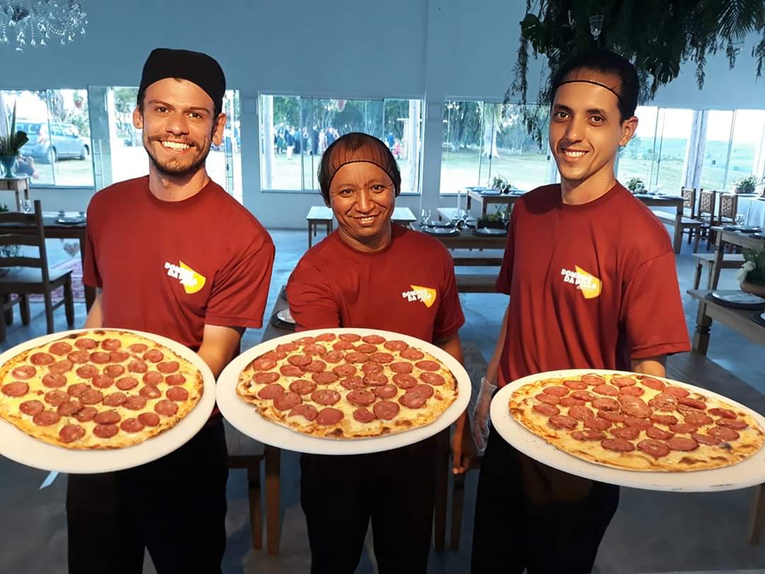 Três pessoas de camisa vermelha estão segurando três pizzas