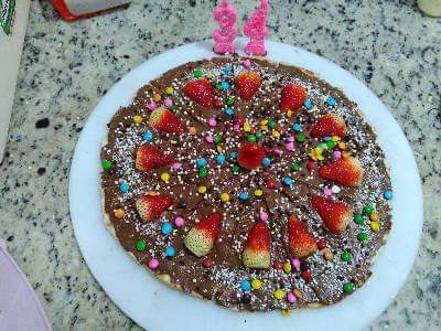 Uma pizza com calda de chocolate, morangos e granulado em um prato.