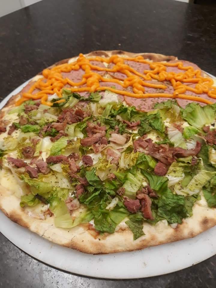 Uma pizza com alface, carne e queijo em um prato branco sobre uma mesa.