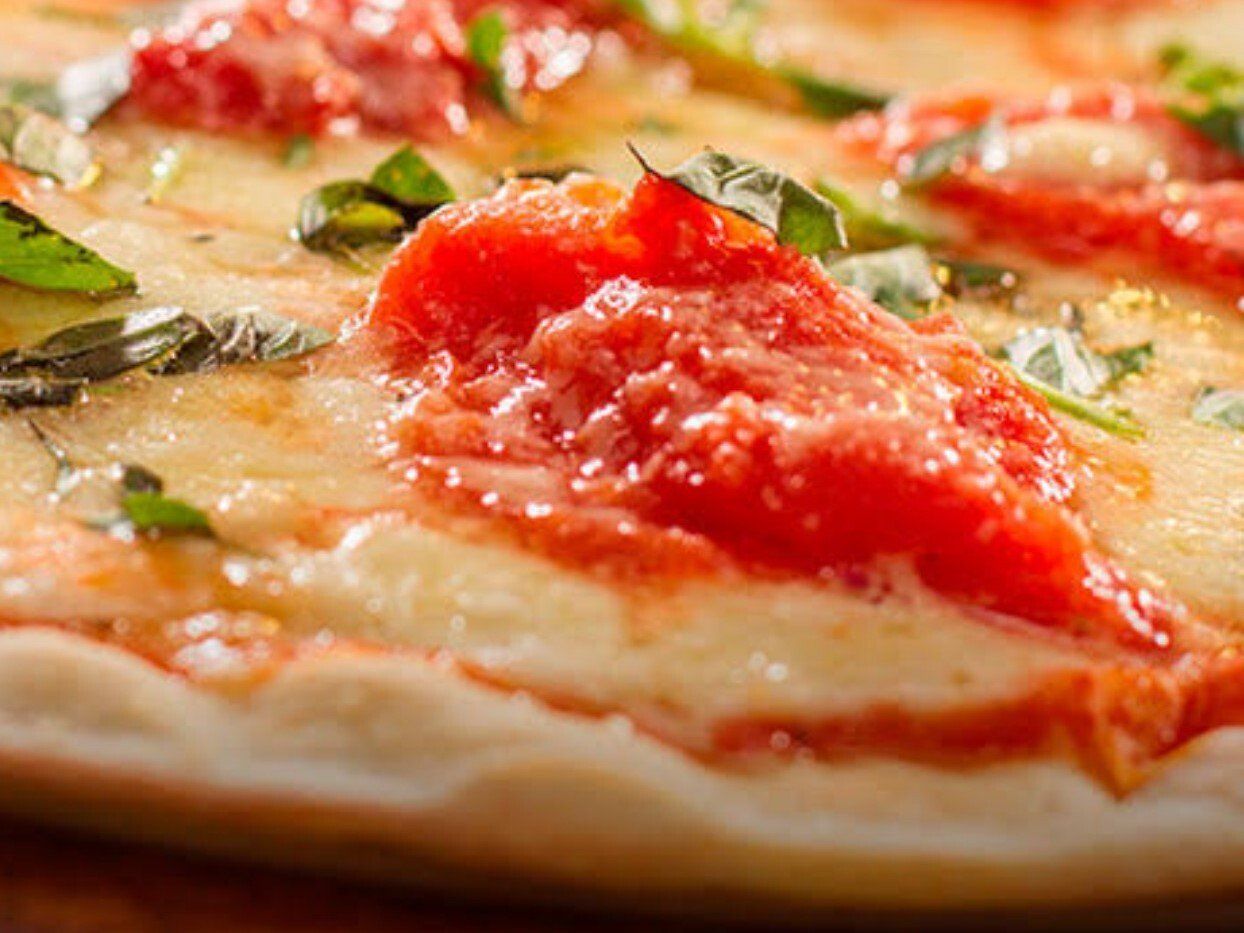 Um close de uma pizza com molho de tomate e manjericão em uma mesa de madeira.