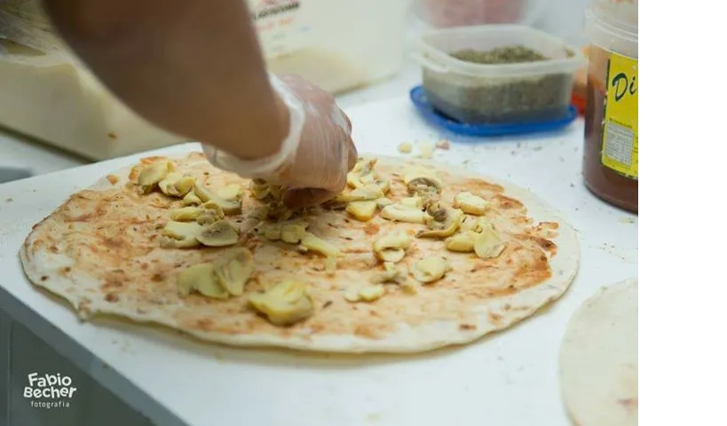 Uma pessoa está colocando cogumelos em uma pizza em uma tábua de corte.