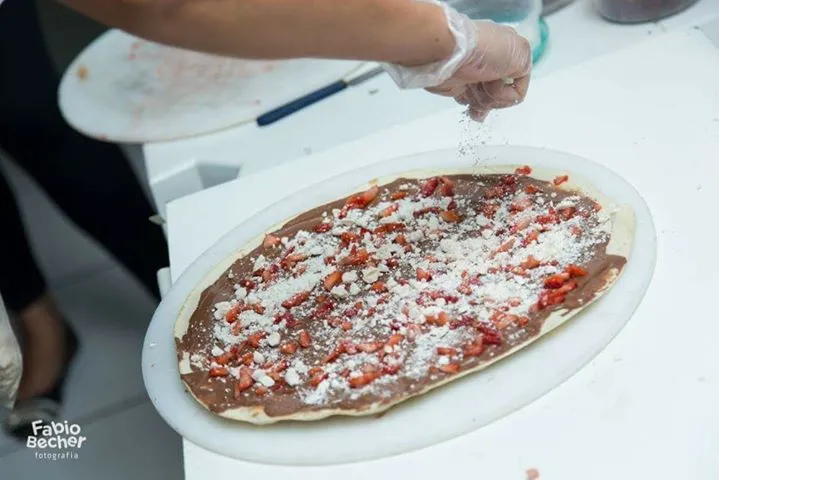 Uma pessoa está espalhando calda de chocolate em uma pizza
