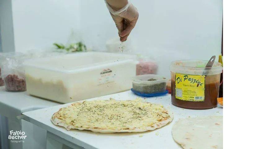 Uma pessoa está espalhando molho em uma pizza sobre uma mesa.