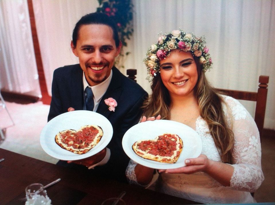 Uma noiva e um noivo segurando pratos de pizza em forma de coração