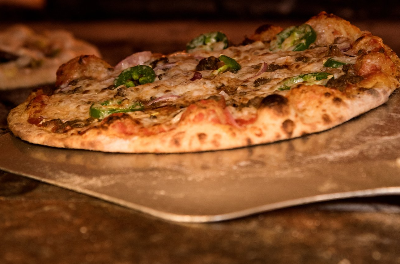 Uma pizza está sendo retirada do forno em uma pá de pizza.