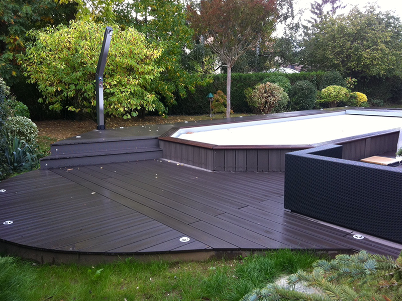 Une terrasse en bois avec une piscine en arrière-plan