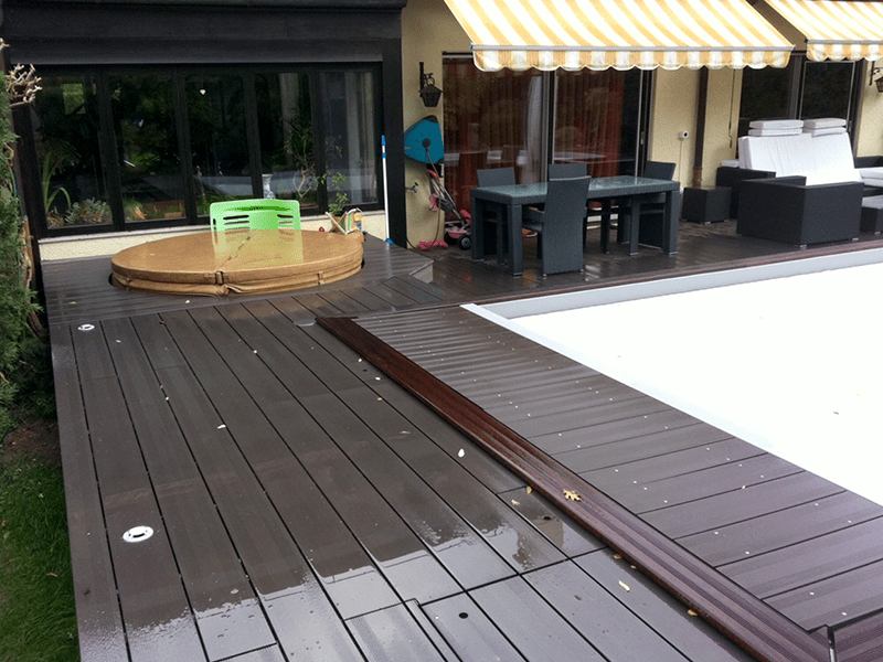 Une terrasse en bois avec une piscine en arrière-plan
