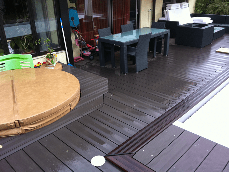 Une terrasse en bois avec une table et des chaises au bord d'une piscine.