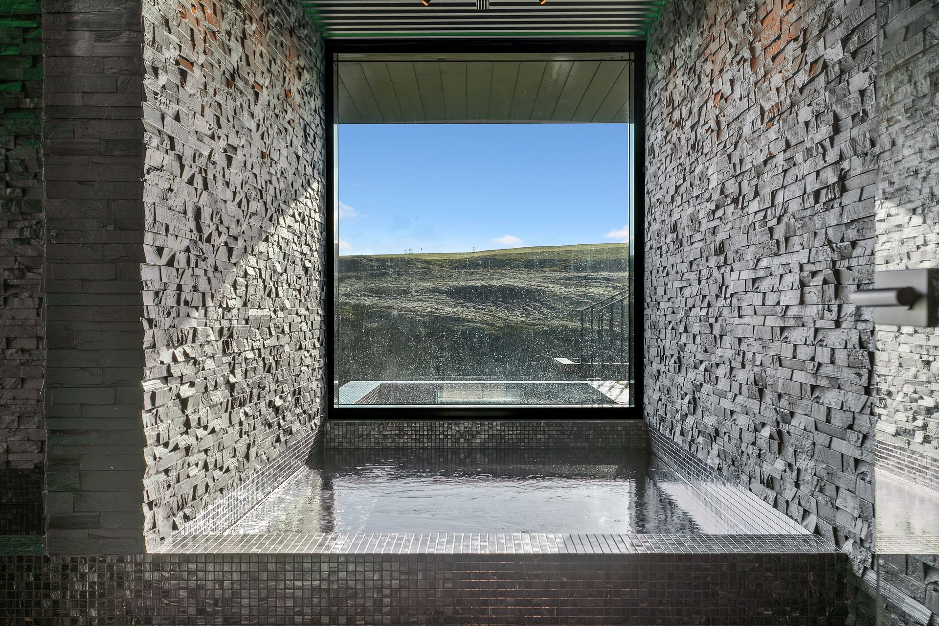 A square stone-tiled hot tub faces a beautiful landscape in Iceland
