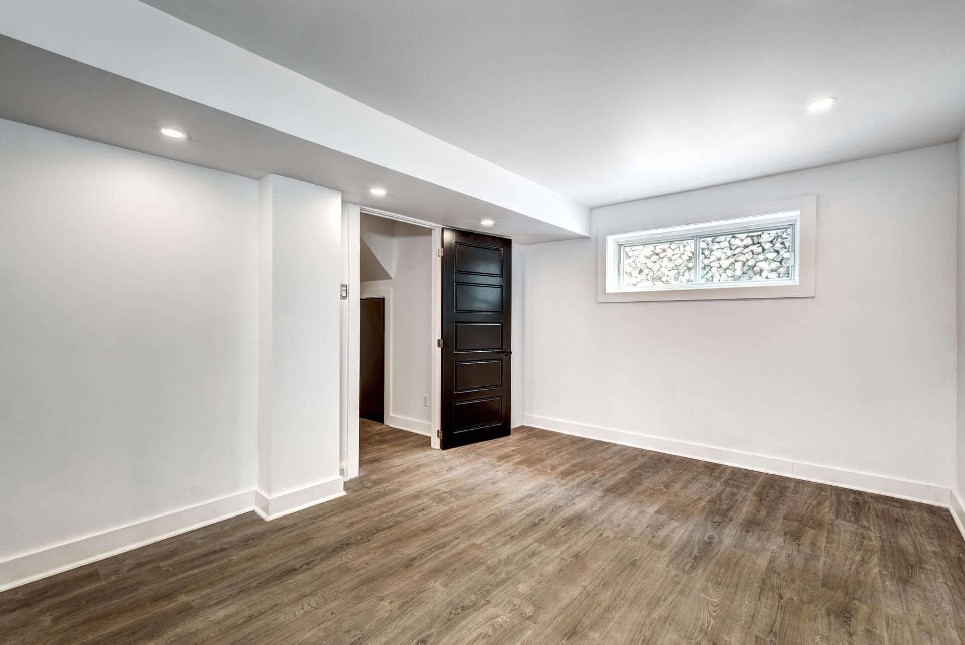 An empty basement with hardwood floors and white walls