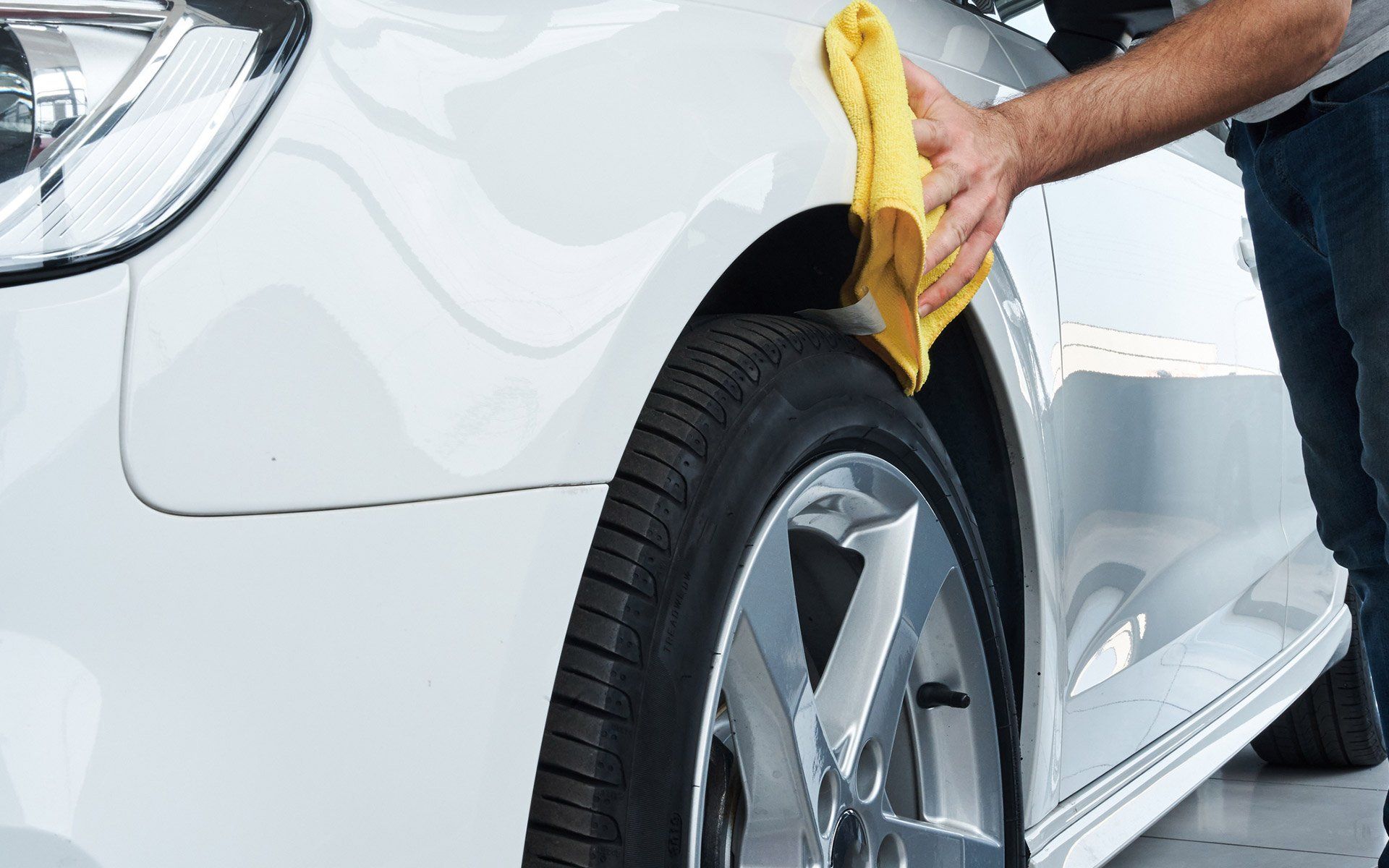 Person wiping a white car’s wheel and fender with a yellow cloth