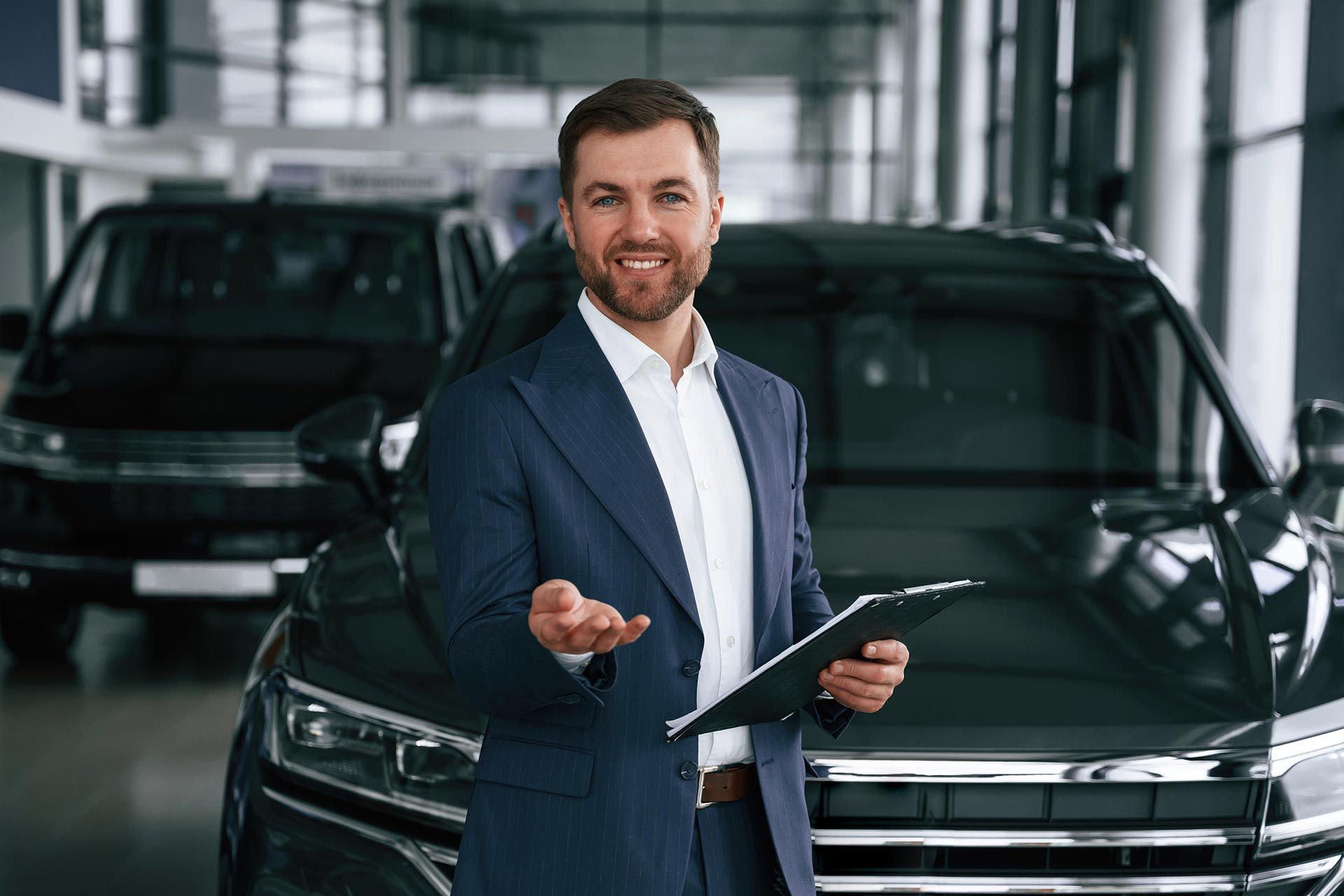 Salesman in a navy suit holding a clipboard in a car showroom, standing beside a black SUV Salesman in a navy suit holding a clipboard in a car showroom, standing beside a black SUV