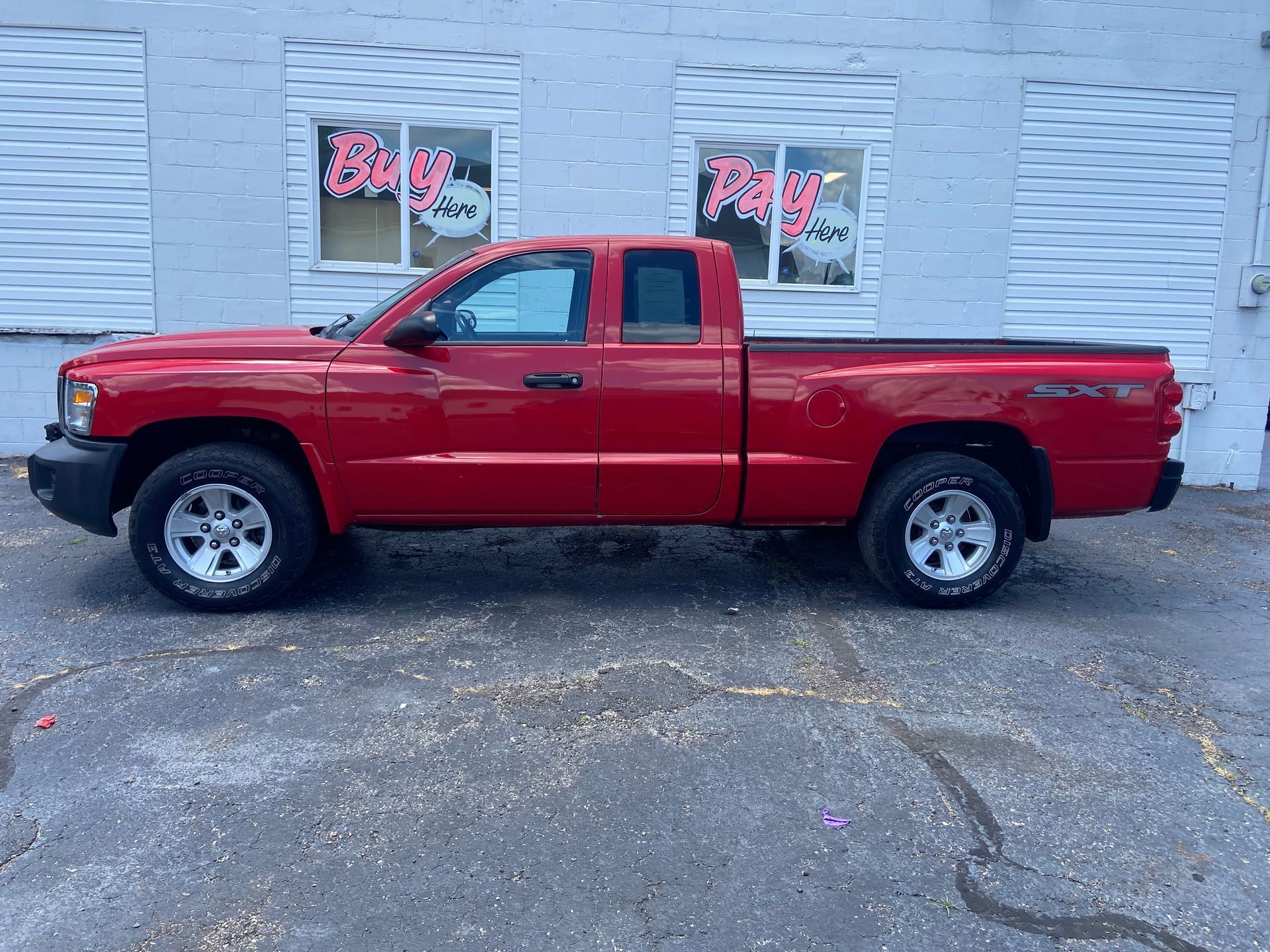 Red pickup truck parked in front of a gray building with windows and pink neon signs.