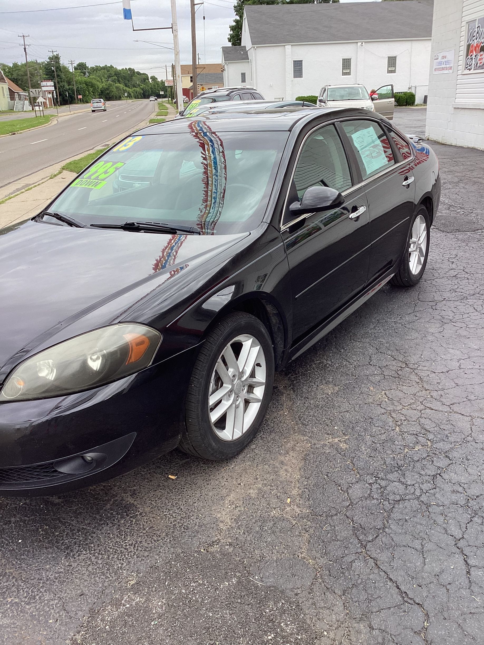 Black sedan parked on a gravel lot beside a road, with white houses in the background.