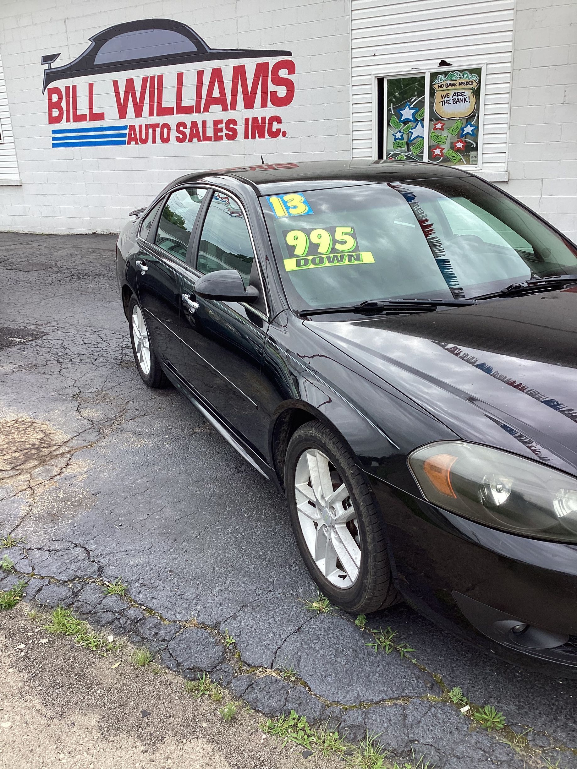 Black sedan parked by Bill Williams Auto Sales with price written on the windshield.