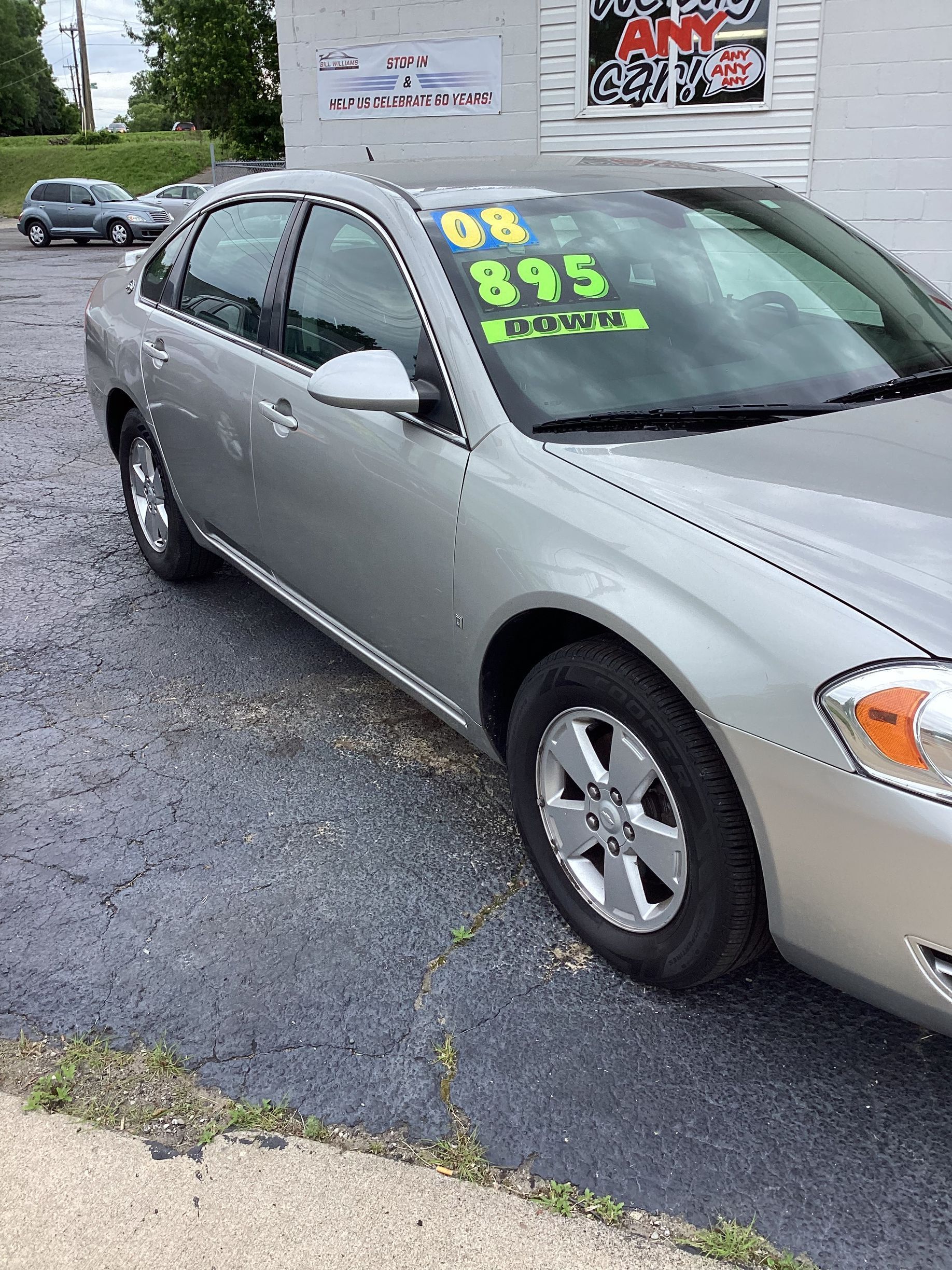 Silver sedan with neon green price and mileage written on the windshield, parked on a lot.